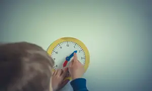 Dziecko uczy się, jak nauczyć dziecko zegara, przesuwając wskazówki na zabawkowej tarczy.