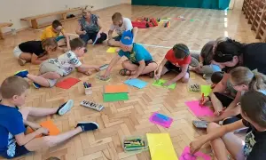 Dzieci klas 1-3 biorą udział w zajęciach plastycznych, rysując na kolorowych kartkach. To część gry i zabawy ruchowej.