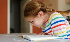 Dziewczynka w okularach z warkoczem pochyla się nad książką. To dowód, jak zachecic dzieci do czytania – wystarczy ciekawa historia!