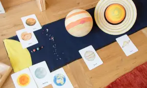 Fascynująca lekcja o kosmosie dla dzieci: karty z planetami, modele Słońca i Jowisza, małe koraliki imitujące gwiazdy.