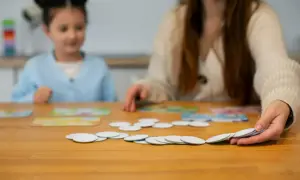 Dziecko i dorosły grają w gry logopedyczne, układając karty na drewnianym stole.