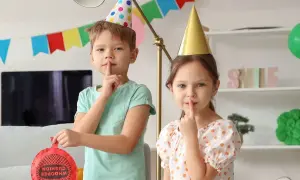 Dzieci w czapkach urodzinowych planują primaaprilisowe psikusy. Chłopiec trzyma poduszkę pierdzącą.