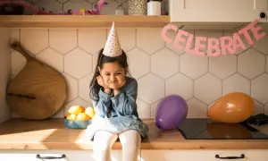 Smutna dziewczynka w czapce urodzinowej zastanawia się, co na urodziny do przedszkola zamiast słodyczy. Balony i napis "CELEBRATE" sugerują przyjęcie.