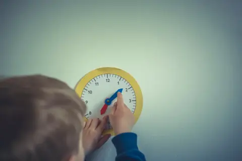 Dziecko uczy się, jak nauczyć dziecko zegara, przesuwając wskazówki na zabawkowej tarczy.