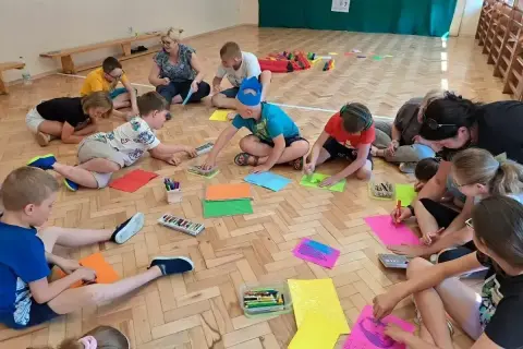 Dzieci klas 1-3 biorą udział w zajęciach plastycznych, rysując na kolorowych kartkach. To część gry i zabawy ruchowej.