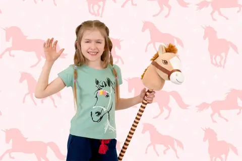 Uśmiechnięta dziewczynka z konikiem na patyku, gotowa do zabawy w hobby horsing na tle różowych jednorożców.