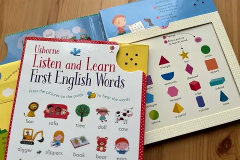 Interaktywne materiały do nauki angielskiego dla dzieci: książka "Listen and Learn First English Words" z obrazkami zwierząt, przedmiotów i kształtów.