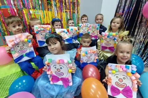 Dzieci w przedszkolu świętują bal karnawałowy, prezentując własnoręcznie wykonane prace z wizerunkami klaunów.