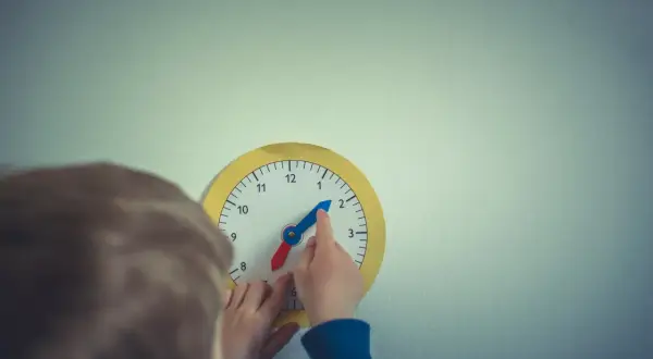 Dziecko uczy się, jak nauczyć dziecko zegara, przesuwając wskazówki na zabawkowej tarczy.