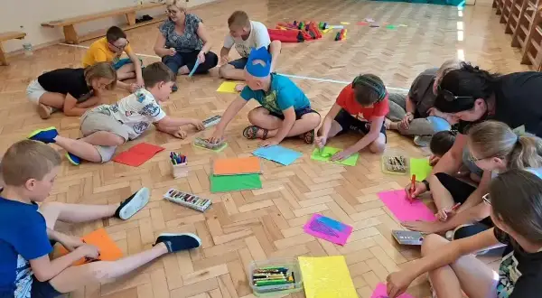 Dzieci klas 1-3 biorą udział w zajęciach plastycznych, rysując na kolorowych kartkach. To część gry i zabawy ruchowej.
