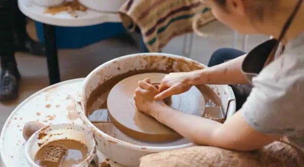 Dzieci tworzą ceramikę na kole garncarskim. Ręce formują glinę, tworząc pierwsze dzieła.