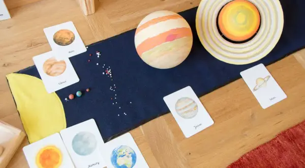 Fascynująca lekcja o kosmosie dla dzieci: karty z planetami, modele Słońca i Jowisza, małe koraliki imitujące gwiazdy.
