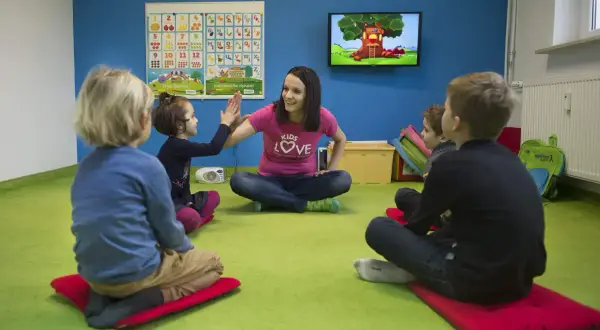 Nauczycielka z uśmiechem przybija piątkę z dziećmi. Wesoła nauka angielskiego dla 4 latka w kolorowej sali.