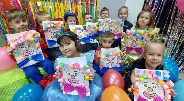 Dzieci w przedszkolu świętują bal karnawałowy, prezentując własnoręcznie wykonane prace z wizerunkami klaunów.
