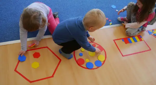 Dzieci układają kolorowe figury geometryczne w wyznaczonych obszarach.