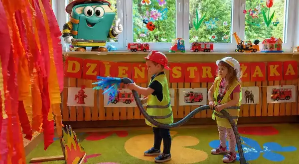 Dzieci w strojach strażaków gaszą pożar, świetne pomysły na animacje dla dzieci! Zabawka-książka w kasku zachęca do zabawy.