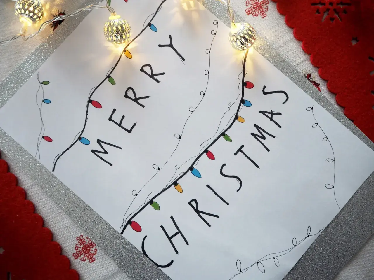 Świąteczne rysunki ołówkiem z kolorowymi lampkami tworzą napis "Merry Christmas".
