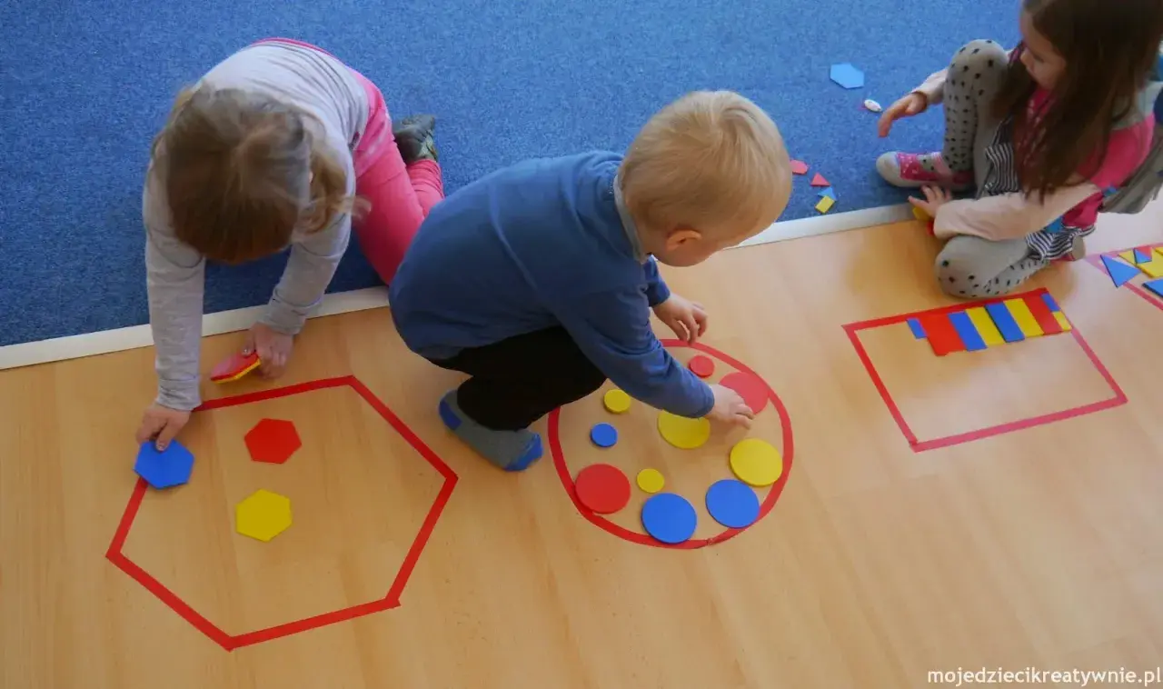 Dzieci układają kolorowe figury geometryczne w wyznaczonych obszarach.