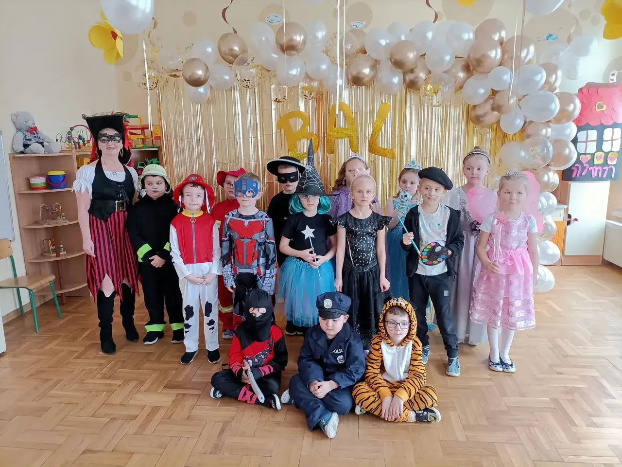 Dzieci w przedszkolu świętują bal karnawałowy w barwnych strojach: piratki, strażaka, ninja, policjanta, tygryska i księżniczki.