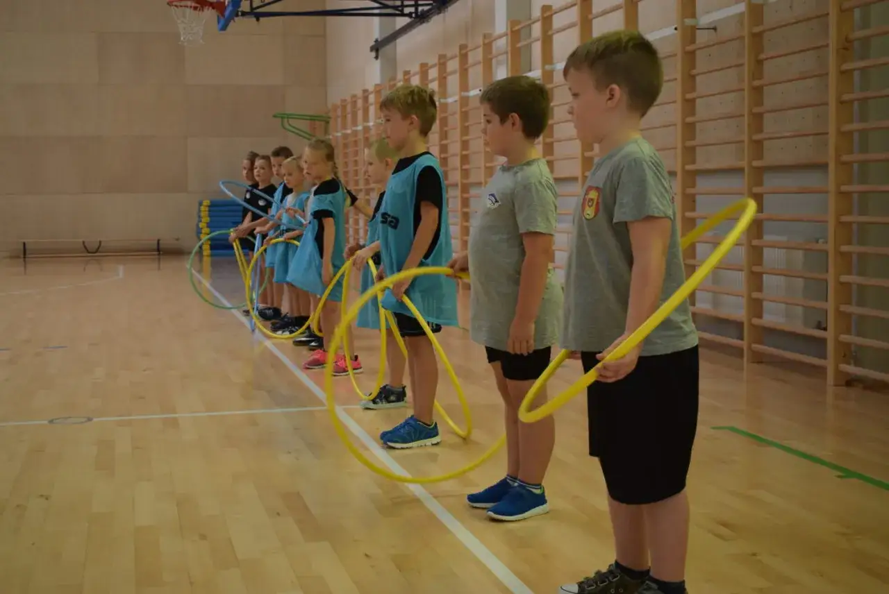 Dzieci z klas 1-3 na sali gimnastycznej, gotowe do gry i zabawy ruchowej z hula-hop.