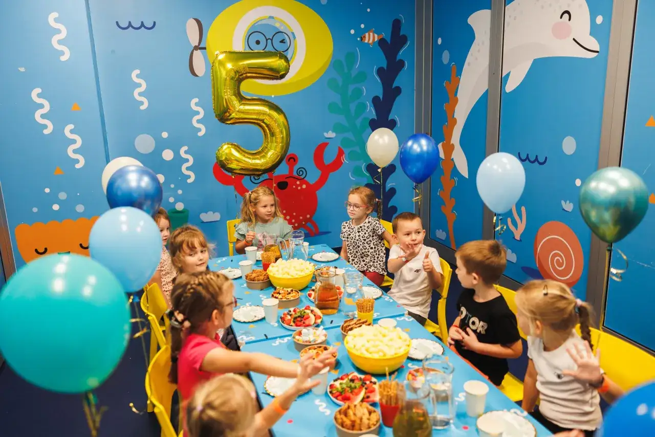Dzieci świętują piąte urodziny przy stole pełnym przekąsek. Balony i morskie dekoracje tworzą fajne atrakcje na urodziny w domu.