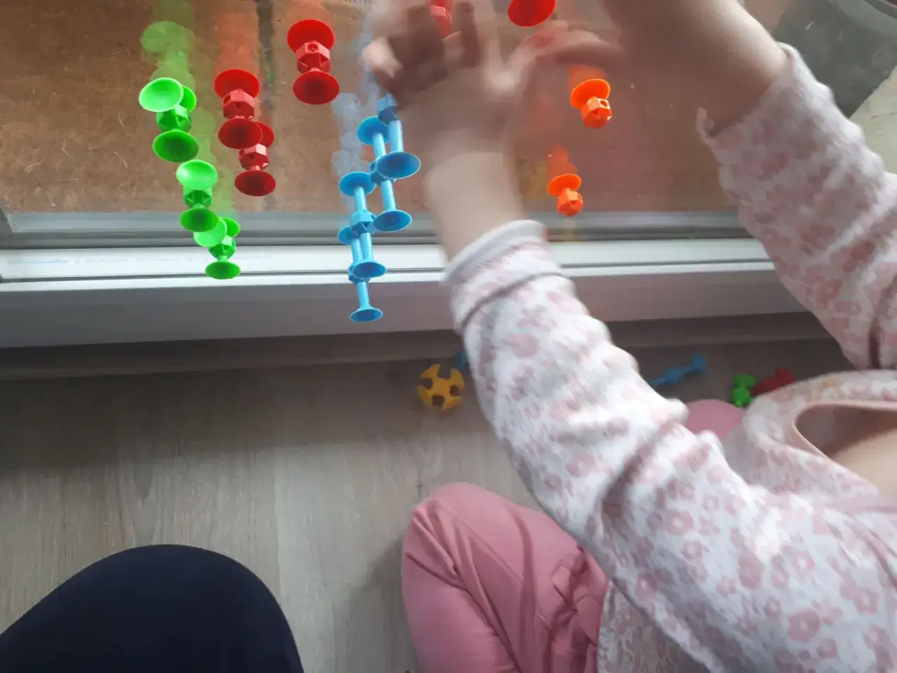 Roczne dziecko bawi się kolorowymi przyssawkami na oknie. To świetne kreatywne zabawy z rocznym dzieckiem, rozwijające motorykę małą.