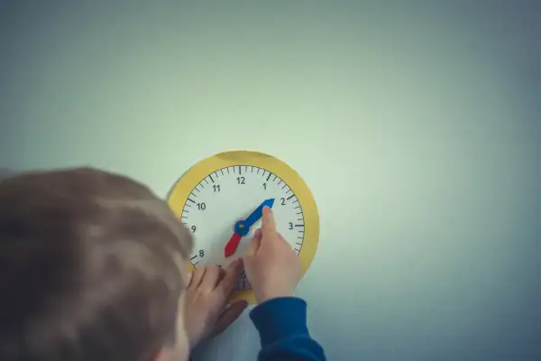 Dziecko uczy się, jak nauczyć dziecko zegara, przesuwając wskazówki na zabawkowej tarczy.