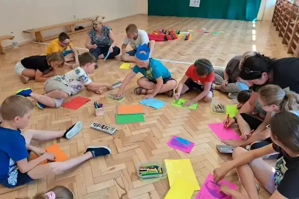 Dzieci klas 1-3 biorą udział w zajęciach plastycznych, rysując na kolorowych kartkach. To część gry i zabawy ruchowej.
