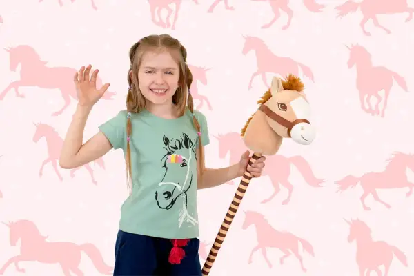 Uśmiechnięta dziewczynka z konikiem na patyku, gotowa do zabawy w hobby horsing na tle różowych jednorożców.