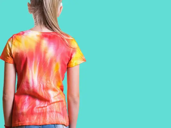 Dziewczynka w koszulce tie dye w odcieniach czerwieni i żółci. Zobacz, jak zrobić tie dye krok po kroku!