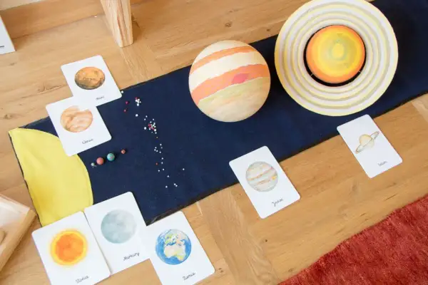 Fascynująca lekcja o kosmosie dla dzieci: karty z planetami, modele Słońca i Jowisza, małe koraliki imitujące gwiazdy.