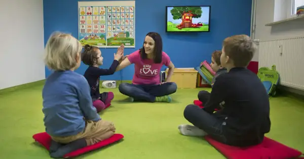 Nauczycielka z uśmiechem przybija piątkę z dziećmi. Wesoła nauka angielskiego dla 4 latka w kolorowej sali.