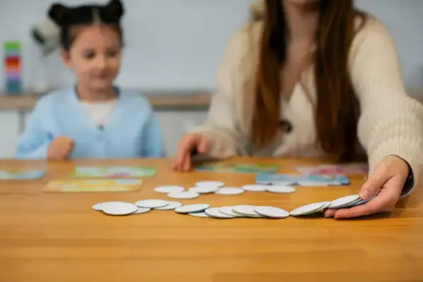 Dziecko i dorosły grają w gry logopedyczne, układając karty na drewnianym stole.
