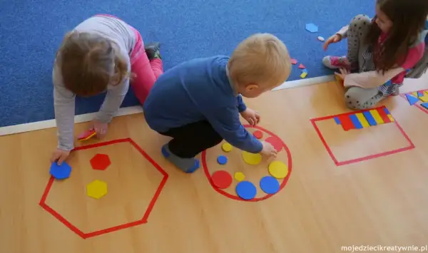 Dzieci układają kolorowe figury geometryczne w wyznaczonych obszarach.