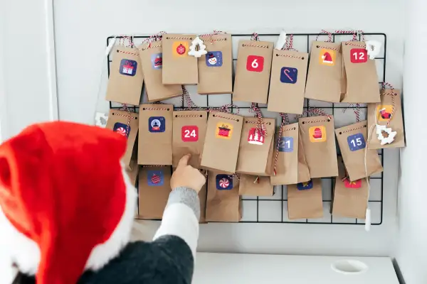 Dziecko w czapce Mikołaja wybiera prezent z kalendarza adwentowego przedszkole. Małe torebeczki ozdobione są świątecznymi naklejkami.