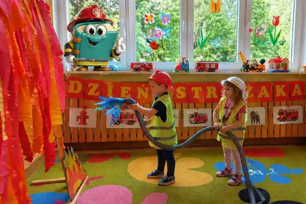 Dzieci w strojach strażaków gaszą pożar, świetne pomysły na animacje dla dzieci! Zabawka-książka w kasku zachęca do zabawy.