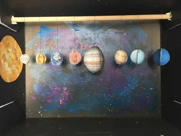 Model układu słonecznego, pokazujący, jak zrobić planety z papieru. Słońce i osiem wiszących planet na tle kosmicznej mgławicy.